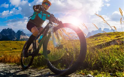 Kobieta na rowerze MTB w górach, słońce przebija się przez chmury. To wolność i przygoda!