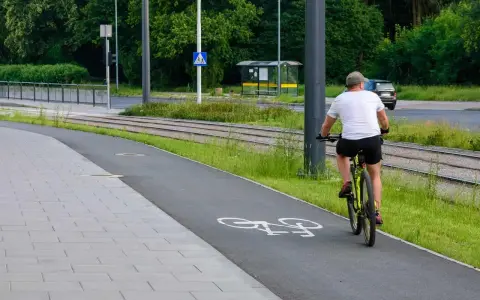 Mężczyzna w czapce i białej koszulce jedzie rowerem po ścieżce. Niebezpieczna jazda rowerem po alkoholu.