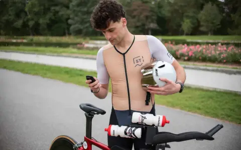 Kolarz sprawdza telefon, trzymając kask. Zastanawia się, co to jest kadencja, gdy patrzy na rower.