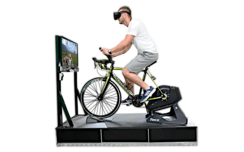 Mężczyzna w goglach VR pedałuje na rowerze stacjonarnym, doświadczając wirtualnej przejażdżki. To zaawansowany symulator jazdy rowerem.