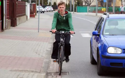 Młody mężczyzna na rowerze jedzie po chodniku, obok drogi. To miejsce, gdzie można jeździć bez karty rowerowej.