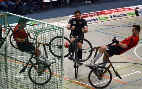 Gracze w piłkę rowerową walczą o piłkę przy bramce. Jeden z zawodników próbuje strzelić gola.