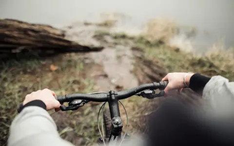 Ręce na kierownicy roweru, błotnista ścieżka i widok na wodę. To właśnie dlatego warto jeździć rowerem – bliskość natury i wolność.