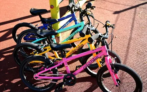 Rowerki dziecięce roko bikes w kolorach: różowym, żółtym, turkusowym i niebieskim, gotowe do zabawy na placu.