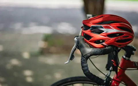Czerwony kask rowerowy i kierownica z owijką. Niezbędne wyposażenie rowerzysty na bezpieczną podróż.