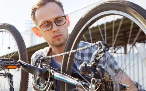 Mężczyzna w okularach sprawdza rozmiary kół rowerowych, skupiony na mechanizmie przerzutek i łańcuchu.