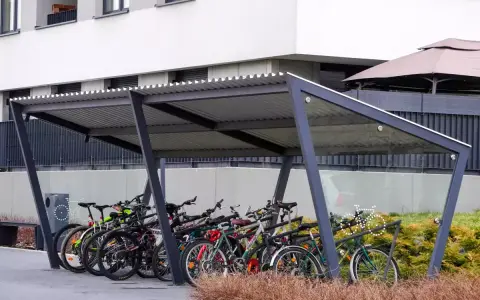 Rzędy rowerów czekają na swoich właścicieli pod nowoczesną wiatą. Bezpieczne przechowywanie roweru na dworze to wygoda i ochrona przed deszczem.