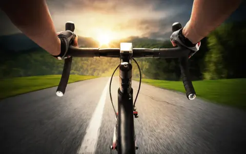 Rowerzysta w rękawiczkach mija pola i lasy, celując w zachód słońca. Dziś na liczniku pojawi się 100 km na rowerze.