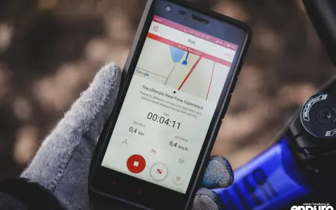 Rękawiczka trzyma smartfon z aplikacją licznik rowerowy. Widoczny czas 00:04:11, dystans 0,4 km i średnia prędkość 6,4 km/h.