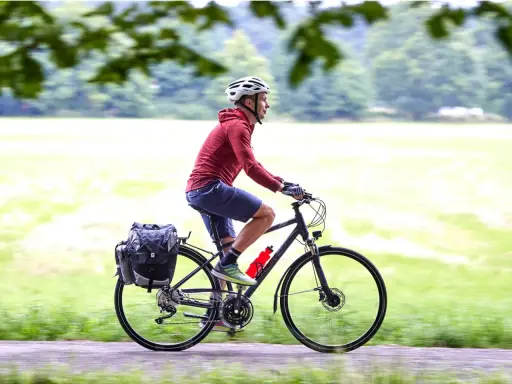 Mężczyzna w kasku jedzie na rowerze trekkingowym z sakwami. Idealny na wycieczki!