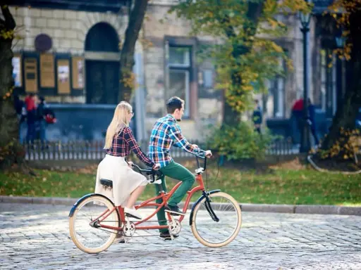 Para co to? Para na rowerze typu tandem przemierza brukowaną uliczkę w jesiennym mieście.