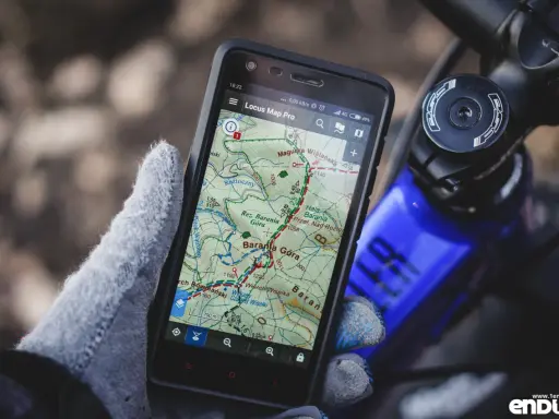 Rękawiczka trzyma smartfon z mapą górską, pokazującą darmowa aplikacja na rower. Idealna do nawigacji w terenie.