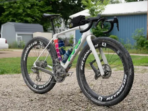 Biały rower gravelowy z szerokimi oponami i sakiewką na kierownicy, gotowy na przygodę. Czy to gravel czy szosa, zależy od terenu!