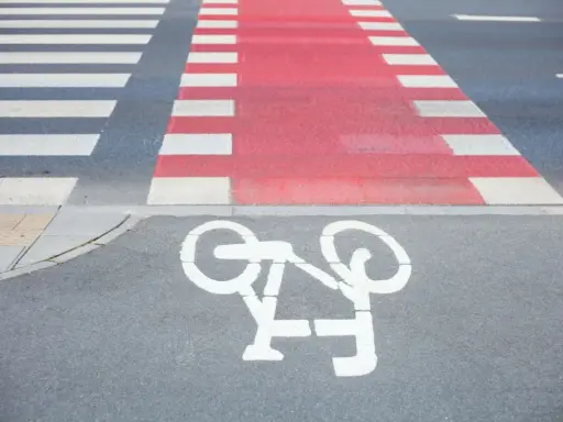 Czerwone pasy dla rowerzystów przecinają przejście dla pieszych. Symbol roweru na asfalcie zaprasza do bezpiecznej jazdy.