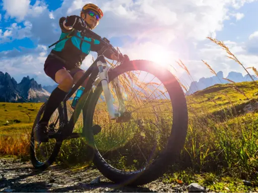 Kobieta na rowerze MTB w górach, słońce przebija się przez chmury. To wolność i przygoda!