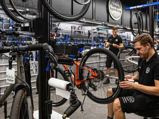 W warsztacie fabryki rowerów mechanik naprawia rower. W tle wiszą rowery i narzędzia.