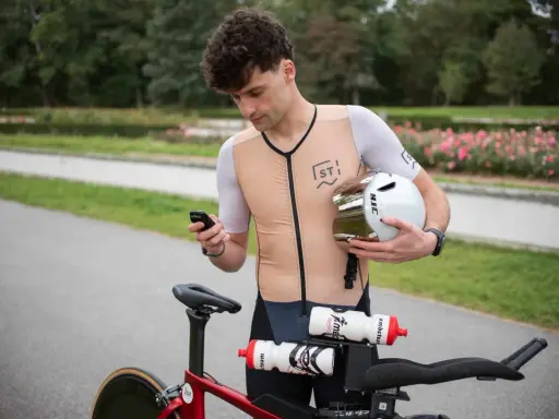 Kolarz sprawdza telefon, trzymając kask. Zastanawia się, co to jest kadencja, gdy patrzy na rower.