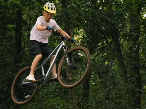 Chłopiec w kasku wykonuje skok na rowerze na leśnej ścieżce. To prawdziwy rower na hopy!
