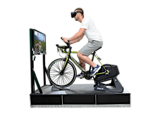 Mężczyzna w goglach VR pedałuje na rowerze stacjonarnym, doświadczając wirtualnej przejażdżki. To zaawansowany symulator jazdy rowerem.