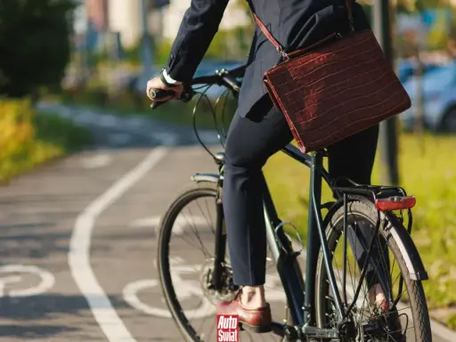 Biznesmen na rowerze z teczką na ramieniu, jadący po ścieżce rowerowej. Czyżby to był zakaz jazdy rowerem w tym miejscu?