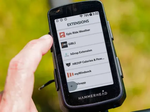 Palec dotyka ekranu Hammerhead Karoo 3, wyświetlającego listę rozszerzeń, w tym Epic Ride Weather i GiBLi.