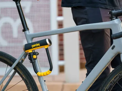 Solidne, żółto-czarne zapięcie rowerowe OnGuard zabezpiecza ramę szarego roweru. To idealne jakie zapięcie do roweru dla każdego rowerzysty.