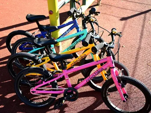 Rowerki dziecięce roko bikes w kolorach: różowym, żółtym, turkusowym i niebieskim, gotowe do zabawy na placu.