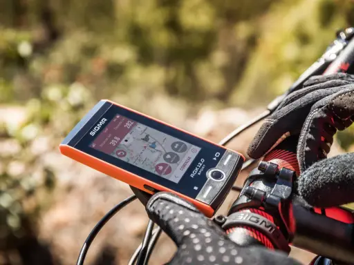 Pomarańczowy licznik rowerowy Sigma ROX 12.0 Sport pokazuje dystans 39.8 km i wysokość 282 m. Rękawiczka rowerowa na kierownicy.