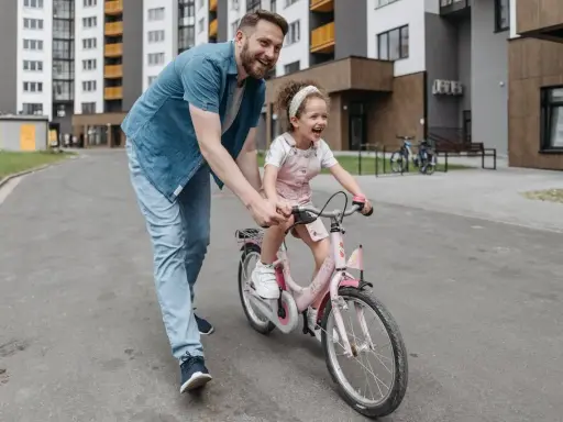 Tata uczy córkę, jak nauczyć dziecko jazdy na rowerze. Radosna dziewczynka na różowym rowerze, tata ją asekuruje.