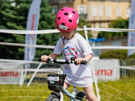 Dziewczynka w różowym kasku na rowerze, z numerem 30. Czy kask na rower dla dziecka jest obowiązkowy? Tak, dla bezpieczeństwa!