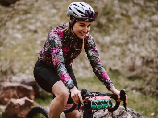 Uśmiechnięta rowerzystka w kwiecistej bluzie pokonuje kolejne kilometry. Dziś cel to 50 km na rowerze po górskich ścieżkach.
