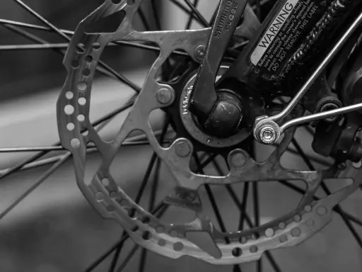 Zbliżenie na tarczę hamulcową i piastę roweru. Widoczne są szprychy, zacisk hamulcowy i dźwignia Shimano. To kluczowe elementy wpływające na przełożenia w rowerze.