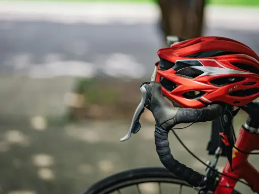 Czerwony kask rowerowy i kierownica z owijką. Niezbędne wyposażenie rowerzysty na bezpieczną podróż.