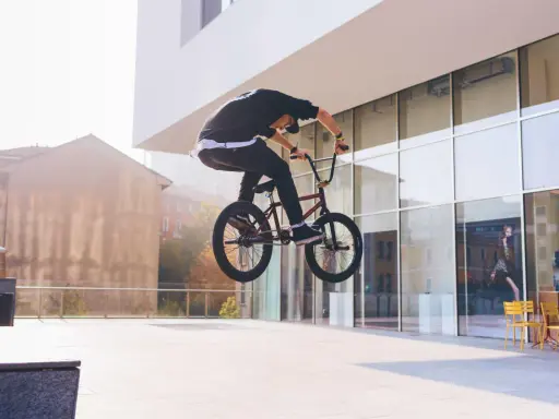 Chłopak na BMX-ie wykonuje bunny hop, unosząc rower w powietrze przed nowoczesnym budynkiem.