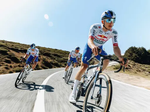 Kolarze jadący w peletonie, pokonując kolejne kilometry Tour de France. Słońce i błękitne niebo towarzyszą im w wyścigu.