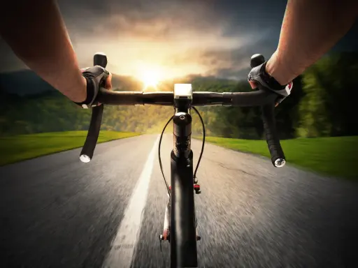 Rowerzysta w rękawiczkach mija pola i lasy, celując w zachód słońca. Dziś na liczniku pojawi się 100 km na rowerze.