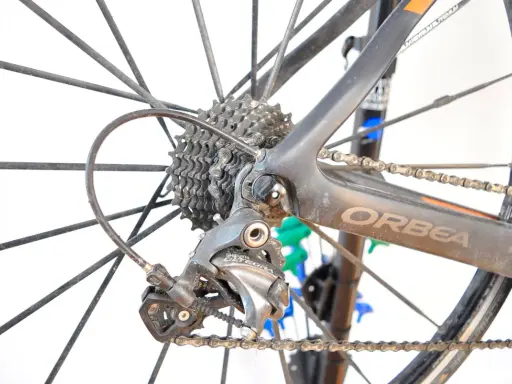 Tylna przerzutka Shimano Ultegra, kluczowy element przekładni rowerowej, na tle koła i ramy Orbea.