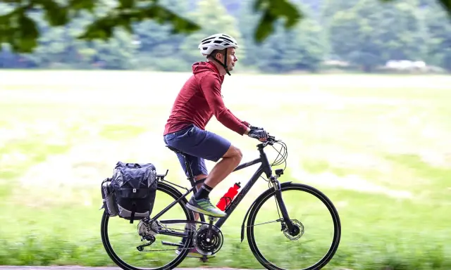 Mężczyzna w kasku jedzie na rowerze trekkingowym z sakwami. Idealny na wycieczki!