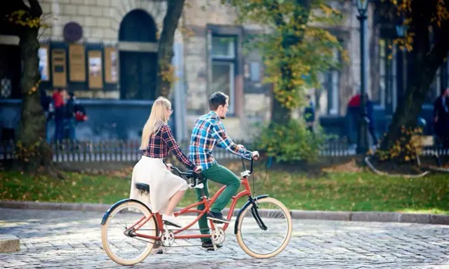 Para co to? Para na rowerze typu tandem przemierza brukowaną uliczkę w jesiennym mieście.