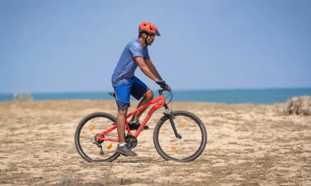 Mężczyzna w kasku jedzie na rowerze po plaży. Sprawdź, co obejmuje gwarancja roweru, by mieć pewność podczas każdej wyprawy.