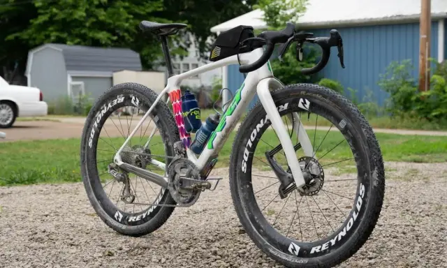 Biały rower gravelowy z szerokimi oponami i sakiewką na kierownicy, gotowy na przygodę. Czy to gravel czy szosa, zależy od terenu!