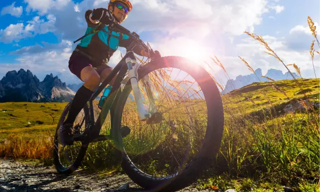 Kobieta na rowerze MTB w górach, słońce przebija się przez chmury. To wolność i przygoda!
