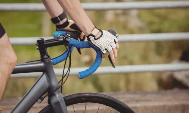Rowerzysta w rękawiczkach trzyma kierownicę. Czas przekroczyć prog mleczanowy i przyspieszyć.