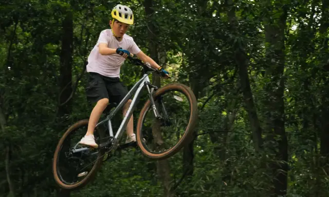 Chłopiec w kasku wykonuje skok na rowerze na leśnej ścieżce. To prawdziwy rower na hopy!