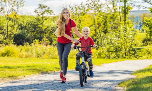 Mama pomaga synkowi w nauce jazdy na rowerze w słoneczny dzień w parku.