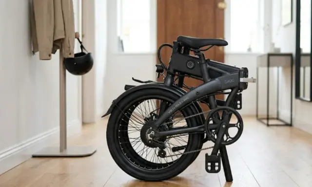 Składany rower elektryczny Volta G400, idealny do miasta. Obok wieszak z kurtką i kaskiem.