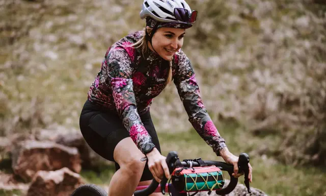 Uśmiechnięta rowerzystka w kwiecistej bluzie pokonuje kolejne kilometry. Dziś cel to 50 km na rowerze po górskich ścieżkach.
