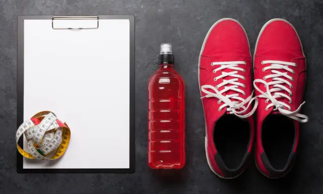 Tabela węglowodanów w produktach, miarka krawiecka, czerwony napój izotoniczny i buty sportowe.