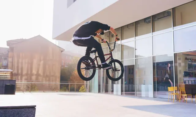 Chłopak na BMX-ie wykonuje bunny hop, unosząc rower w powietrze przed nowoczesnym budynkiem.