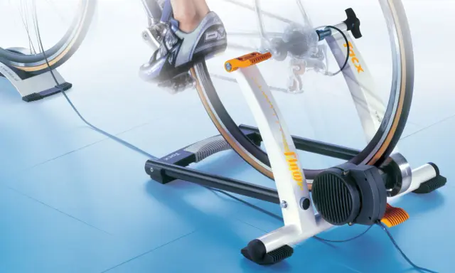 Trenażer rowerowy pozwala ćwiczyć jazdę na rowerze w domu. Widoczny rower jest zamontowany na urządzeniu, które symuluje jazdę.
